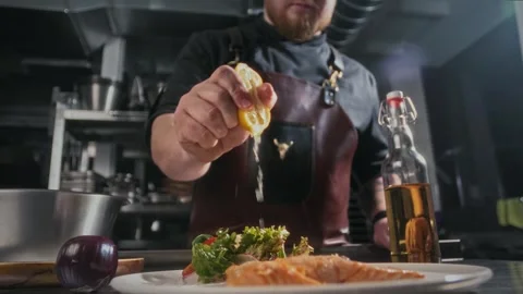 Chef squeezes juice from half a lemon with hands onto delicious fried fish dish Stock Footage 315230374