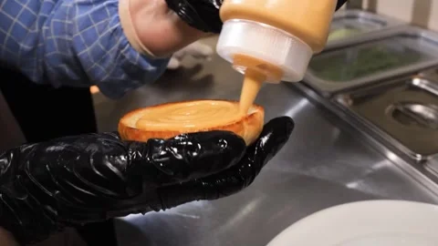 Chef Squeezing Creamy Burger Sauce onto a Toasted Bun for Gourmet Hamburger Prep Stock Footage 331633221