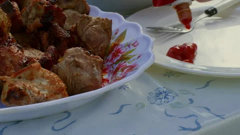Chef squeezing ketchup from a bottle onto a plate near a dish of grilled meat 動画素材 296722355