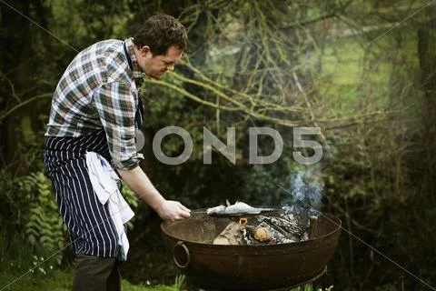 Chef standing in a garden, grilling a fish on a barbecue. Stock-Fotos