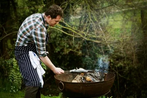 Chef standing in a garden, grilling a fish on a barbecue. Stock Photos