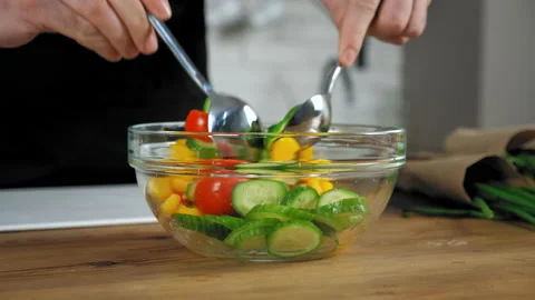Chef standing near kitchen table mix vegetarian salad with spoons in glass bowl Stock Footage 148091302