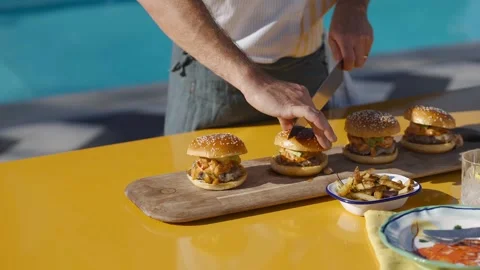 The chef stands behind a kitchen table, deftly cutting burgers in half Stock Footage 247054618