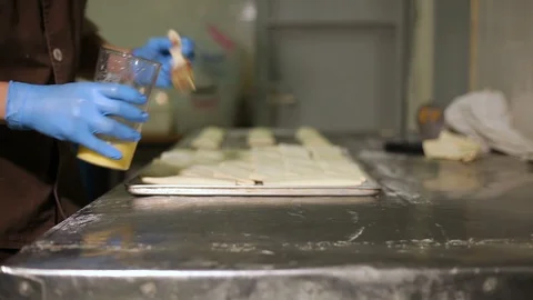 Chef on a steel table greases rolls with egg on a baking sheet Stock Footage 106478053