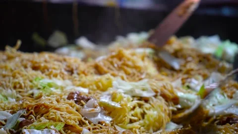 Chef stir-frying massive yakisoba noodles on hot griddle Stock Footage 346503536
