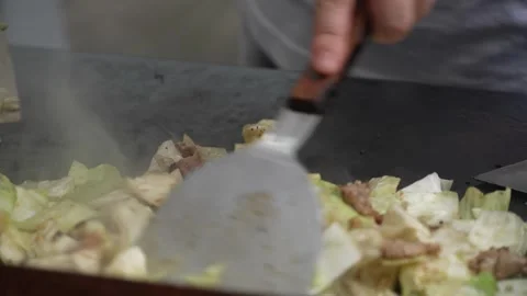 Chef stir-frying meat and cabbage on hot griddle with spatulas Stock Footage 346503373