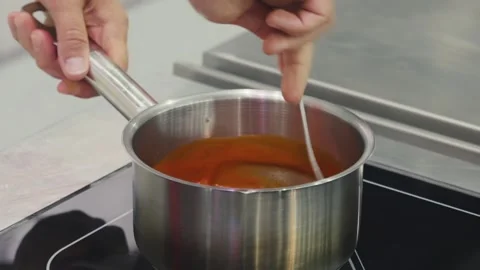 Chef stiring fruit mash with a spoon in stainless steel pot on electric stove Stock Footage 304317471