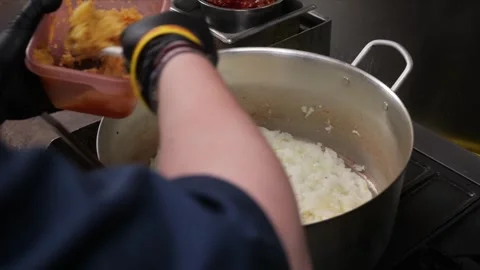 Chef stirring chopped onions in a large pot, preparing a meal Stock Footage 331634142