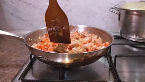 Chef stirring diced pork meat with tomatoes and onions in a pan Stockbeeldmateriaal 334758525