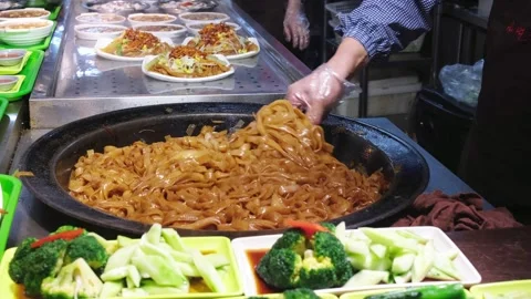 Chef stirring noodles in large flat pan at street food stall 動画素材 336320870