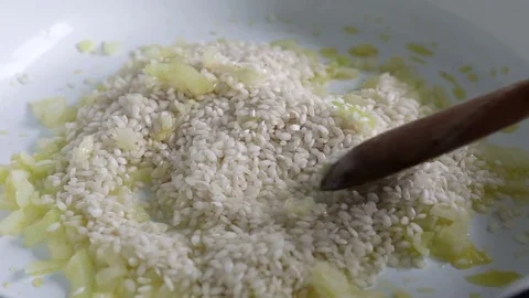 Chef stirring risotto rice with onions and garlic, frying on white ceramic pan 動画素材 78734224