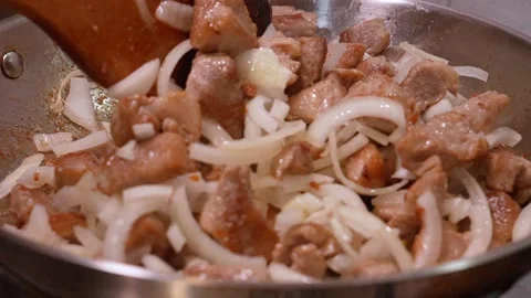 Chef stirring sizzling pork and onions in pan Vidéo 335136363