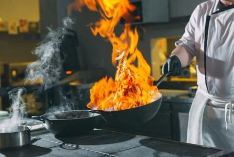 Chef is stirring vegetables in work on the kitchen. Stock Photos