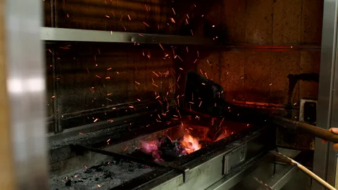 Chef Stirs Hot Charcoal in Restaurant Grill with Sparks Flying in Commercial Stock Footage 337720372