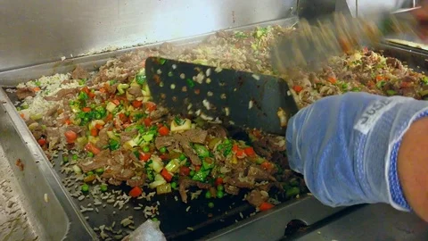 A Chef Stirs Large Portion of Beef, Rice &amp; Vegetables On Large Grill Stock Footage 73805963