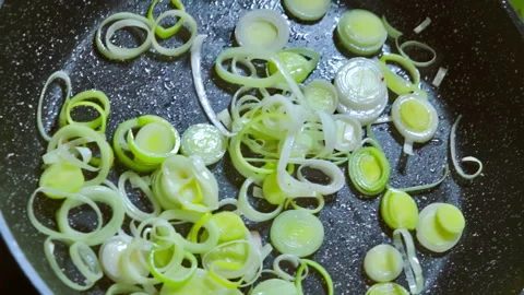 A chef stirs sliced leeks while frying them in a pan with olive oil. Stock Footage 309299999
