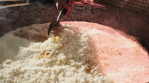 The chef stirs steaming rice in a large pilaf cauldron with a slotted spoon Stock Footage 254638823