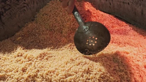 The chef stirs steaming rice in a large pilaf cauldron with a slotted spoon Stock Footage 254640324