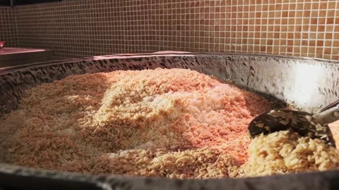 The chef stirs steaming rice in a large pilaf cauldron with a slotted spoon Stock Footage 255932954
