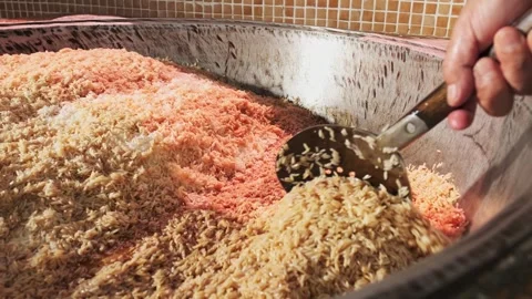The chef stirs steaming rice in a large pilaf cauldron with a slotted spoon Stock Footage 277384542