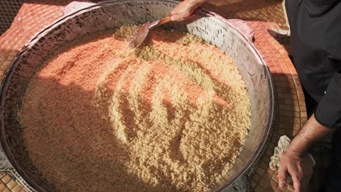 The chef stirs steaming rice in a large pilaf cauldron with a slotted spoon Stock Footage 280461952