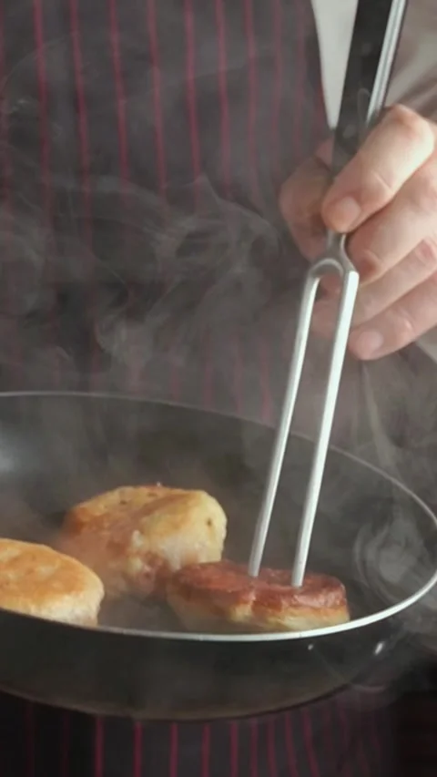 A chef in a striped apron skillfully flips golden brown doughnuts with a fork in Vídeos de archivo 339633802