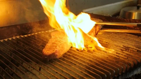 Chef taps steaks on flame grill with tongs and moves meat around Stock-Footage 94247686