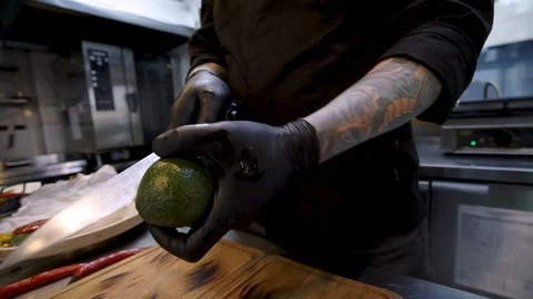 Chef with tattoo in black chef tunic and black rubber gloves peeling avocado  Видео 105272036