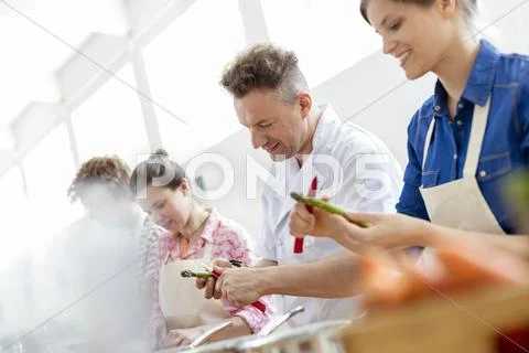 Chef teacher and students peeling asparagus in cooking class kitchen Stock Photos