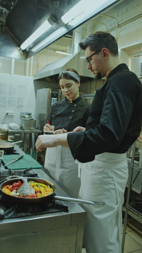 Chef Telling How to Cook Dish to Female Apprentice Taking Notes in Kitchen Stock Footage 270182767