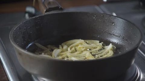 Chef throws chili peppers in a hot pan with fried onions standing on stove. 库存影片 124709766