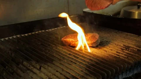 Chef throws on hamburger meat next to steak on flame grill Stock Footage 94247713