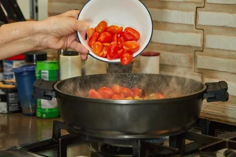 Chef throws tomatoes into a frying pan on a gas stove Stock Photos