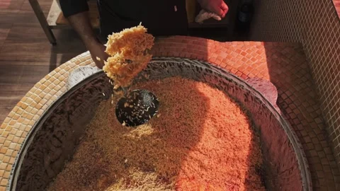 The chef tosses rice with a slotted spoon in a large cauldron while cooking Stock Footage 263101448