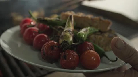 The chef transfers fried fish, tomatoes and vegetables from the grill to a plate Stock Footage 254564851