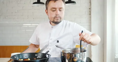 Chef tries checking his food that is cooking in pan on stove, controls condition Stock Footage 133392430