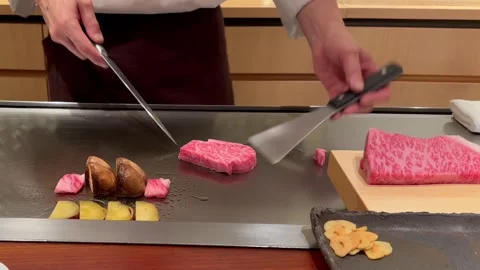 Chef trims fat from Kobe A5 beef on teppan with mushrooms and sliced vegetables Stock Footage 323928281