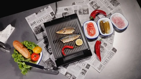 The chef turns two mackerel fillet, lemon and Chilean pepper on a electric grill Stock Footage 128291683