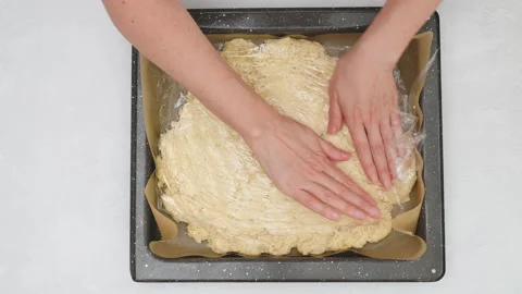 Chef unfurl pizza dough onto a baking pan using a plastic wrap. Stock Footage 148017425