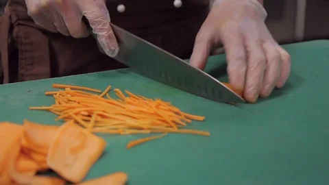 Chef in uniform cuts knife thinly julienned carrots on table. Stock Footage 79973657