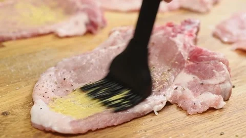 Chef use culinary brush to apply mustard on a raw pork chop. Video stock 195531050