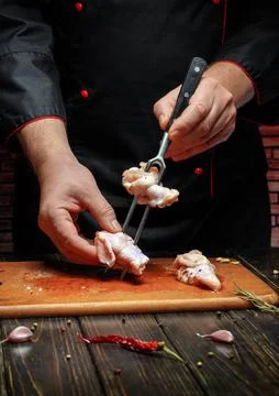 A chef uses a fork to hold and cut meat pieces on a wooden cutting board. The Stock Photos