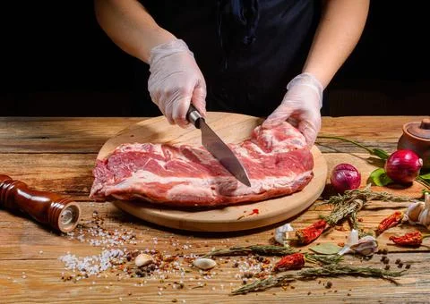 The chef uses his hands to slice pork ribs with a knife on a wooden cutting t Stock Photos