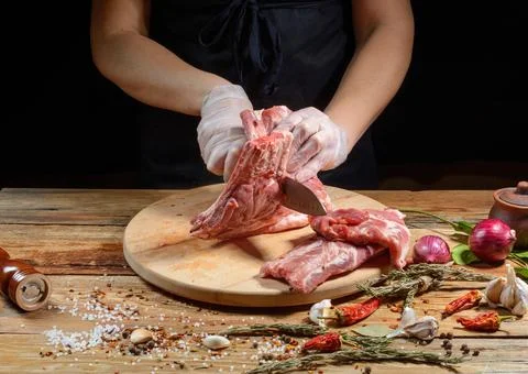 The chef uses his hands to slice pork ribs with a knife on a wooden cutting t Stock Photos