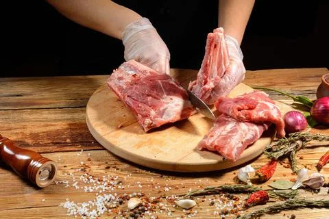 The chef uses his hands to slice pork ribs with a knife on a wooden cutting t Stock Photos