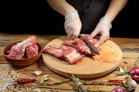 The chef uses his hands to slice pork ribs with a knife on a wooden cutting t Stock Photos