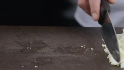 A chef uses a knife to push a pile of sliced onions onto a wooden cutting board. Stock Footage 303404981
