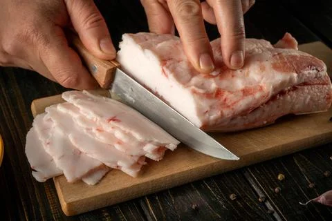 A chef uses a knife to slice raw lard placed on a wooden cutting board in t.. Stock Photos