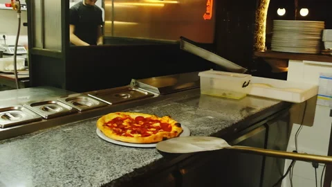 Chef uses long-handled pizza peel to place pizza on plate Video stock 326370157