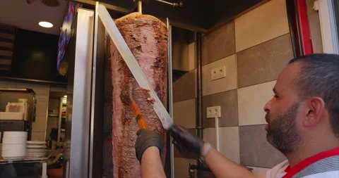 The chef uses a long knife to cut meat for shawarma from a meat block roasting Stock Footage 231717076